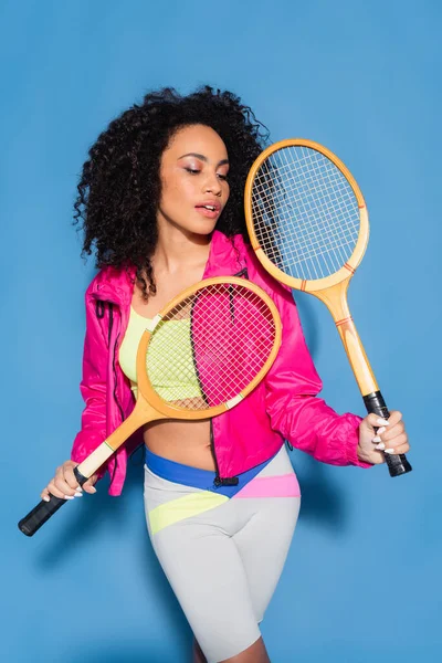 Giovane donna afroamericana che tiene racchette da tennis su blu — Foto stock