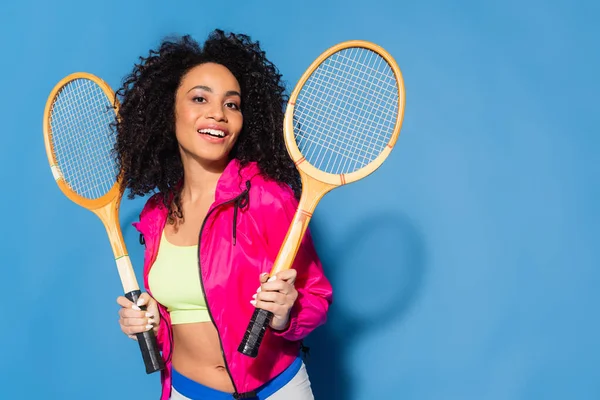 Щаслива молода афроамериканка тримає тенісні ракетки на синьому — стокове фото