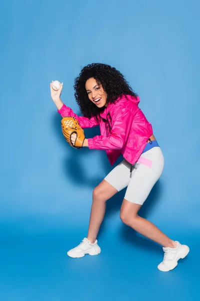 Piena lunghezza di eccitata donna afro-americana che gioca a baseball su blu — Foto stock