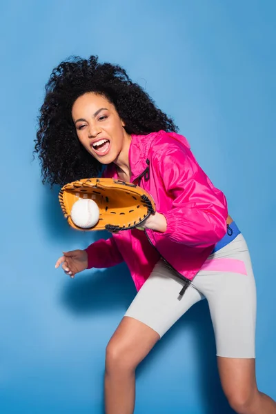 Excited african american woman in leather glove catching baseball on blue — Stock Photo