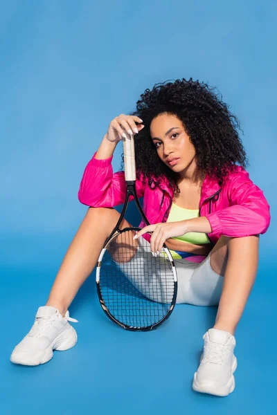 African american woman holding tennis racket while sitting on blue — Stock Photo