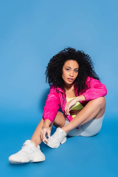 Mujer afroamericana en chaqueta rosa sentada sobre azul - foto de stock