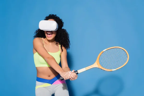 Amazed african american woman in vr headset playing tennis on blue — Stock Photo