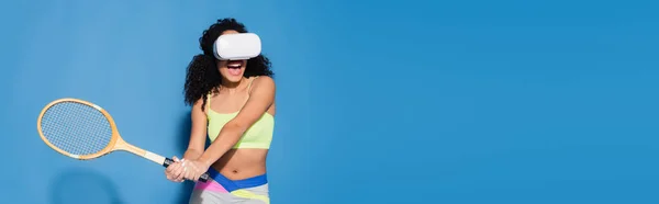 Mujer afroamericana sorprendida en auriculares vr jugando al tenis en azul, bandera - foto de stock