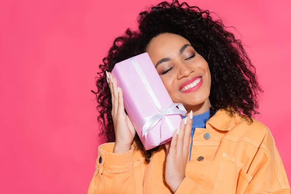 Feliz africana americana mujer en chaqueta celebración presente en rosa - foto de stock