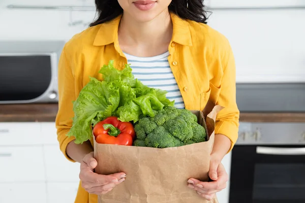 Cropped view of young woman holding paper bag with groceries — Stock Photo