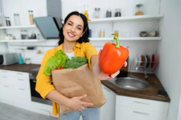 Verschwommen und fröhlich brünette Frau hält Papiertüte mit Lebensmitteln und Paprika — Stockfoto