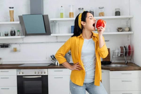 Joven morena mujer con los ojos cerrados mordiendo pimiento rojo - foto de stock