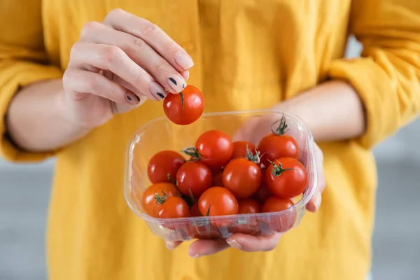 Vista ritagliata di giovane donna in possesso di contenitore di plastica con pomodori ciliegia maturi — Foto stock