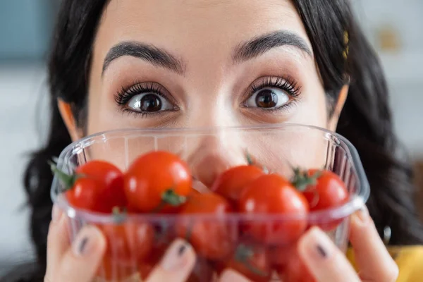 Surprised young woman holding plastic container with ripe cherry tomatoes on blurred foreground — Stock Photo