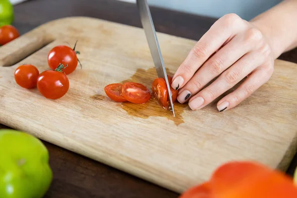 Vue recadrée d'une femme coupant des tomates cerises rouges sur une planche à découper en bois — Photo de stock