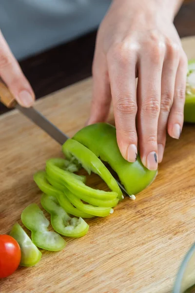 Close up of woman cutting green bell pepper near cherry tomato on chopping board — Stock Photo