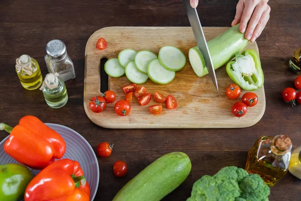 Top view of woman cutting zucchini near cherry tomatoes on chopping board — Stock Photo