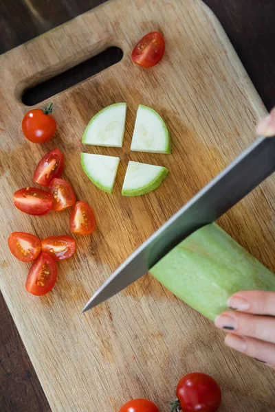 Vue de dessus de la femme coupant des courgettes près de tomates cerises tranchées sur planche à découper — Photo de stock