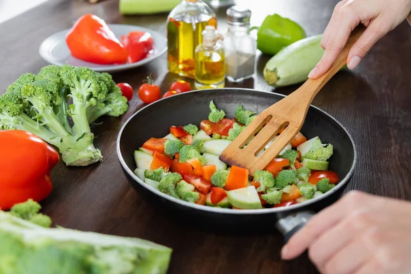 Обрезанный вид женщины, смешивающей нарезанные овощи на сковороде с лопаткой — стоковое фото
