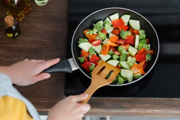 Vista de ángulo alto de la mujer joven mezclando verduras en rodajas en la sartén con espátula - foto de stock