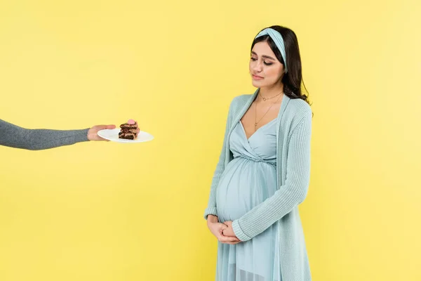 Pregnant woman doubting near piece of cake isolated on yellow — Stock Photo