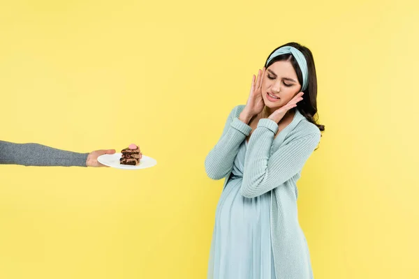 Pregnant woman feeling disgust near piece of delicious cake isolated on yellow — Stock Photo
