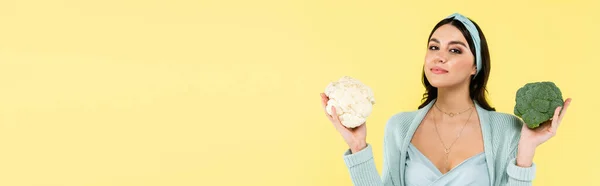 Беременная женщина с цветной капустой и брокколи глядя на камеру изолированы на желтый, баннер — стоковое фото