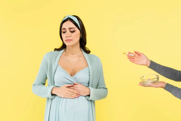 Young pregnant woman touching tummy near ashtray and cigarette isolated on yellow — Stock Photo