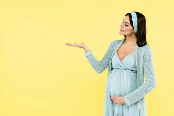 Mujer embarazada sonriente señalando con la mano aislada en amarillo - foto de stock