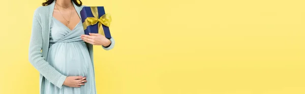 Vista ritagliata della donna incinta che tocca la pancia mentre tiene la scatola regalo isolata su giallo, banner — Foto stock
