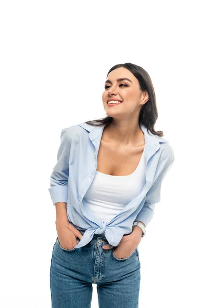 Mujer alegre mirando hacia otro lado mientras posando con las manos en bolsillos aislados en blanco - foto de stock