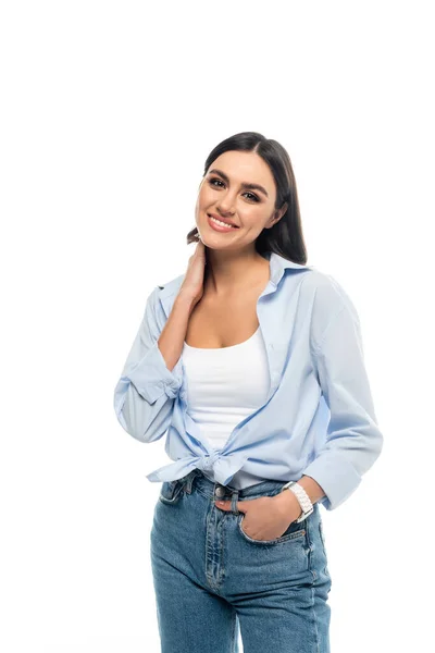 Happy woman in blue shirt touching neck while posing with hand in pocket isolated on white — Stock Photo