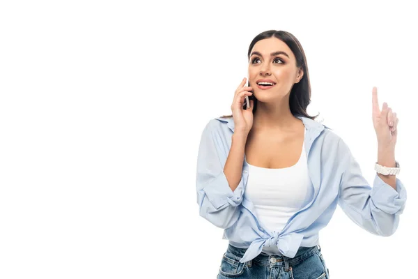 Mujer excitada apuntando hacia arriba con el dedo mientras habla en el teléfono celular aislado en blanco - foto de stock