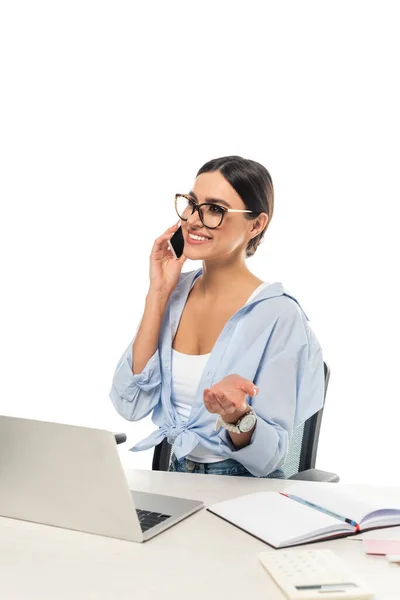 Sonriente mujer de negocios hablando en el teléfono móvil cerca del ordenador portátil aislado en blanco - foto de stock