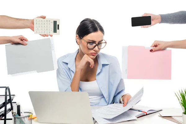 Donna d'affari premurosa che lavora vicino a colleghi con documenti, calcolatrice e smartphone isolati su bianco — Foto stock