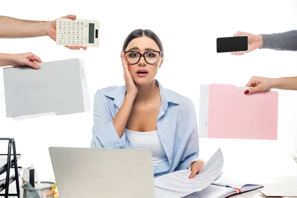 Shocked businesswoman looking at camera near devices and coworkers with documents isolated on white — Stock Photo