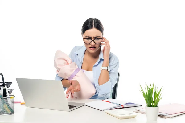 Joven mujer de negocios hablando en el teléfono inteligente mientras está sentado cerca de la computadora portátil con bebé bebé aislado en blanco - foto de stock