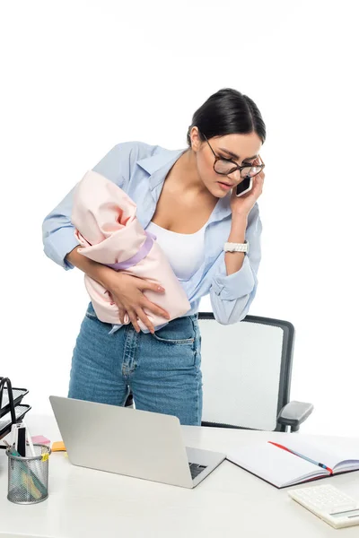 Young mother talking on cellphone while holding baby near work desk isolated on white — Stock Photo