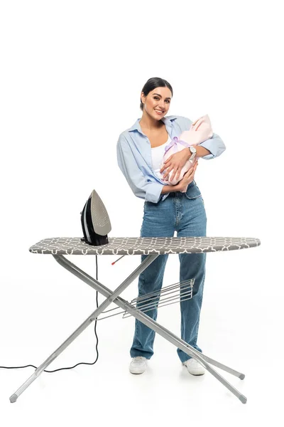 Madre feliz sosteniendo bebé recién nacido cerca de tabla de planchar sobre fondo blanco - foto de stock