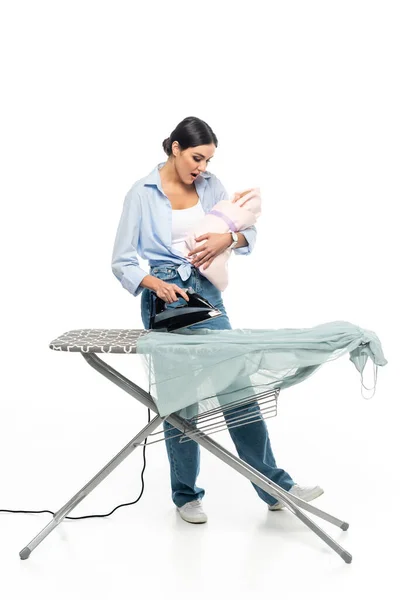 Joven madre cantando a bebé niño mientras plancha ropa sobre fondo blanco - foto de stock