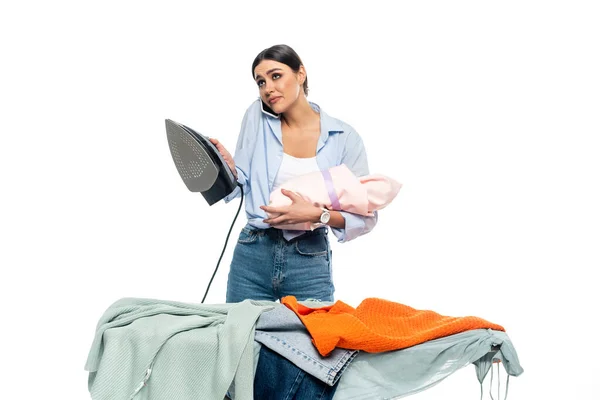 Femme épuisée parlant sur téléphone portable tout en tenant fer et nouveau-né isolé sur blanc — Photo de stock