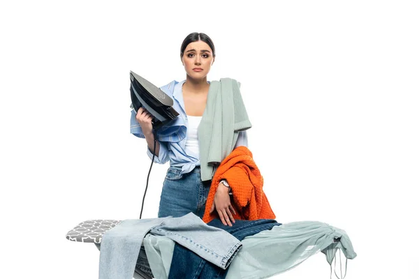 Upset woman holding broken iron near ironing board and clothes isolated on white — Stock Photo
