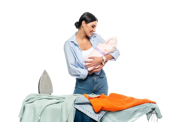 Joven madre sonriendo a bebé bebé cerca de tabla de planchar aislado en blanco - foto de stock