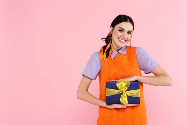 Cheerful woman showing present while looking at camera isolated on pink — Stock Photo