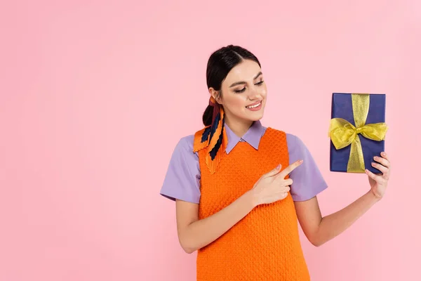 Lächelnde Frau zeigt mit dem Finger auf Geschenkbox in rosa — Stockfoto