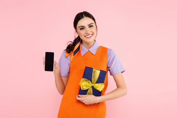 Mulher feliz com caixa de presente mostrando smartphone com tela em branco isolado em rosa — Fotografia de Stock