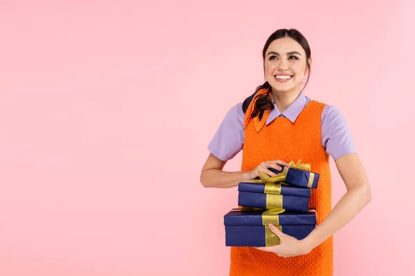 Aufgeregte Frau schaut weg, während sie Geschenkboxen isoliert auf rosa hält — Stockfoto