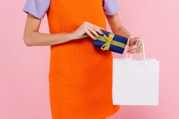 Partial view of woman holding gift box and shopping bag isolated on pink — Stock Photo