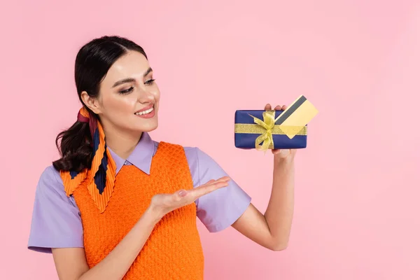 Freudige Frau zeigt auf Geschenkbox und Kreditkarte isoliert auf rosa — Stockfoto