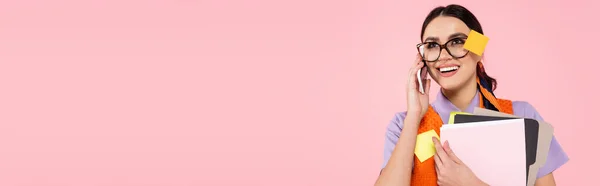 Happy businesswoman holding folders and talking on mobile phone isolated on pink, banner — Stock Photo