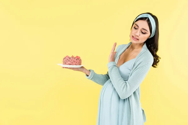 Mujer embarazada mostrando gesto de basura mientras sostiene postre dulce aislado en amarillo - foto de stock