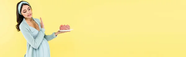 Donna incinta in possesso di torta gustosa e mostrando gesto di rifiuto isolato su giallo, banner — Foto stock