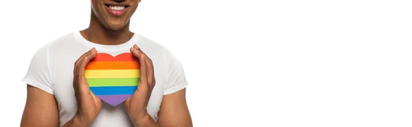 Vue recadrée de souriant homme afro-américain avec des couleurs lgbt coeur en papier isolé sur blanc, bannière — Photo de stock