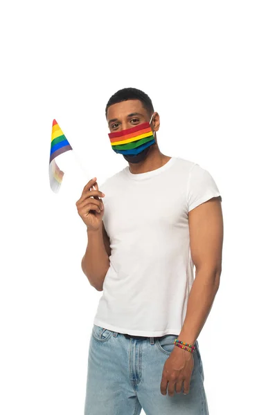 Afrikanisch-amerikanischer Mann mit kleiner LGBT-Fahne und medizinischer Maske in Regenbogenfarben, der isoliert auf weiß in die Kamera blickt — Stockfoto